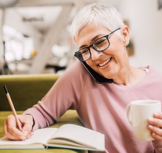Frau mit Brille telefoniert und macht gleichzeitig Notizen.